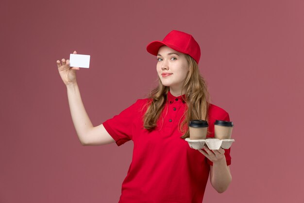 Mensajero femenino en uniforme rojo con café y tarjeta blanca en el servicio uniforme rosa