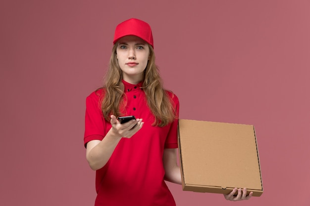 Mensajero femenino en uniforme rojo con caja de comida de entrega y teléfono en rosa claro, trabajador de servicio de trabajo uniforme chica de entrega