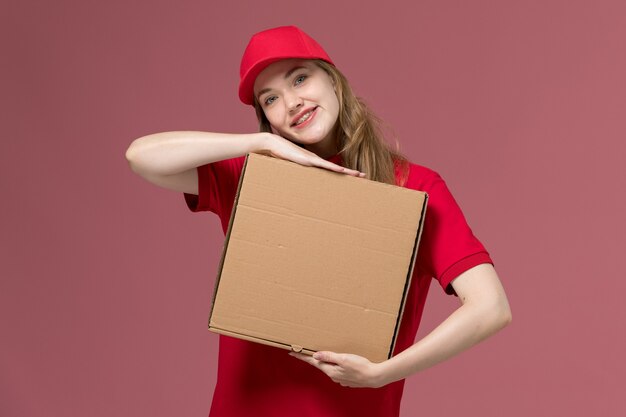 Mensajero femenino en uniforme rojo con caja de entrega de alimentos sonriendo en rosa, trabajo de entrega de servicio uniforme