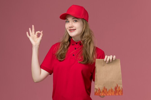 Mensajero femenino en uniforme rojo con paquete de comida de entrega marrón en el trabajador de trabajo de entrega de servicio uniforme rosa
