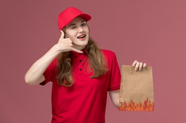 Mensajero femenino en uniforme rojo con paquete de comida de papel en rosa claro, servicio de trabajo uniforme de entrega del trabajador