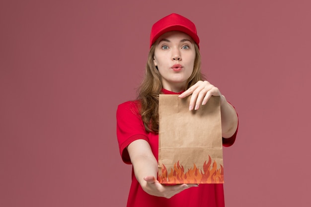Mensajero femenino en uniforme rojo que sostiene el paquete de alimentos en rosa, entrega de servicio de trabajador uniforme de trabajo