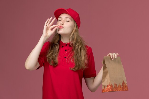 Mensajero femenino en uniforme rojo que sostiene el paquete de comida de papel en la entrega de servicio de trabajador uniforme de trabajo rosa