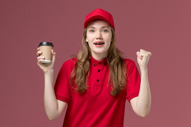 Mensajero femenino en uniforme rojo que sostiene la taza de café de entrega marrón en la entrega de trabajador de servicio uniforme de trabajo de color rosa claro