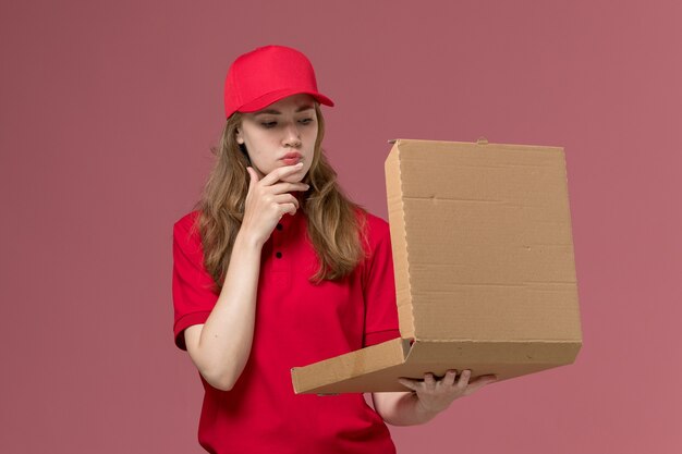 Mensajero femenino en uniforme rojo sosteniendo y abriendo la caja de entrega en rosa claro, servicio uniforme de trabajo entrega del trabajador