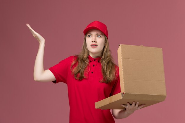 Mensajero femenino en uniforme rojo sosteniendo la apertura de la caja de entrega de alimentos en rosa, trabajo de entrega de servicio uniforme