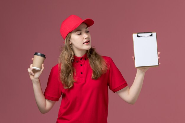 Mensajero femenino en uniforme rojo sosteniendo el bloc de notas y la taza de café en rosa, entrega de servicio de trabajador uniforme de trabajo