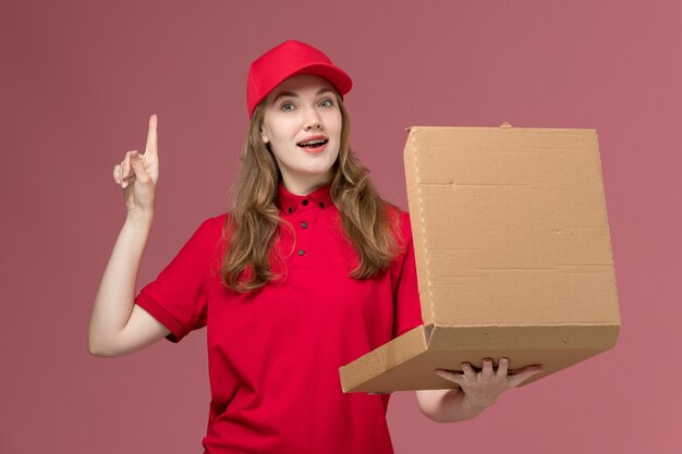 Mensajero femenino en uniforme rojo sosteniendo la caja de comida de entrega abriéndola en rosa claro, servicio uniforme de trabajo entrega de trabajador