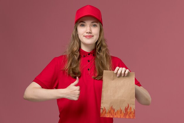 Mensajero femenino en uniforme rojo sosteniendo el paquete de papel de alimentos en rosa, servicio de trabajador de trabajo uniforme entrega