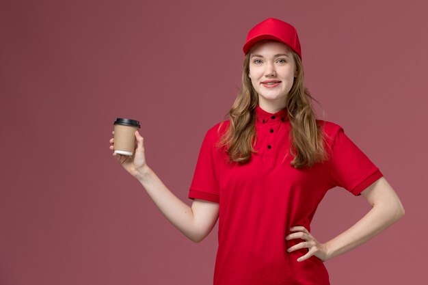 Mensajero femenino en uniforme rojo sosteniendo la taza de café de entrega con una sonrisa posando en rosa, servicio de entrega de servicio de trabajador uniforme de trabajo