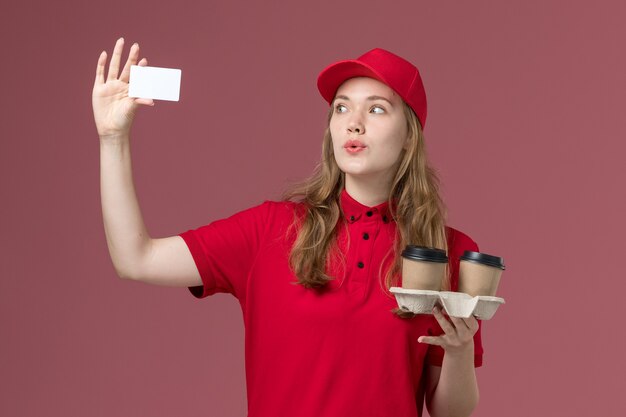 Mensajero femenino en uniforme rojo con tarjeta blanca y café en el servicio uniforme rosa