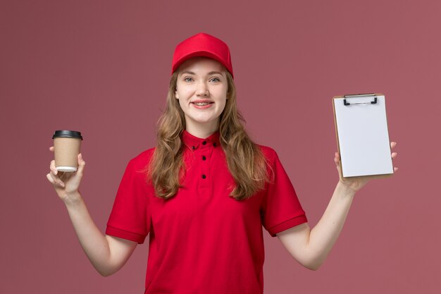 Mensajero femenino en uniforme rojo con taza de café de entrega marrón y bloc de notas en rosa, trabajador de trabajo de entrega de servicio uniforme