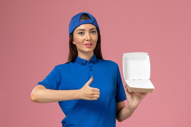 Mensajero femenino de vista frontal con capa uniforme azul sosteniendo pequeños paquetes de entrega vacíos en la pared rosa, trabajo de entrega de la empresa de servicios para empleados