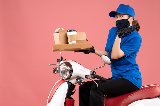 Foto gratuita mensajero femenino de vista frontal en máscara con entrega de alimentos en el rosa