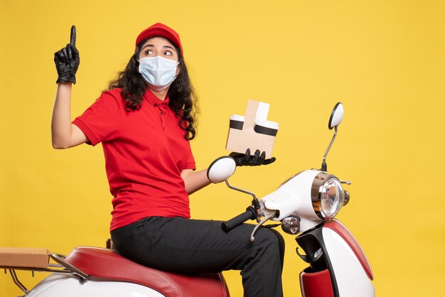 Mensajero femenino de vista frontal en máscara con tazas de café sobre fondo amarillo covid- trabajador uniforme de entrega de trabajo