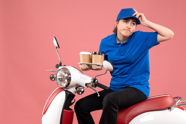 Mensajero femenino de vista frontal sentado en bicicleta con tazas de café en el servicio de comida de trabajador de entrega uniforme de color de trabajo rosa