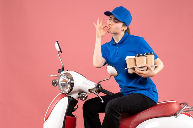 Mensajero femenino de vista frontal sentado en bicicleta con tazas de café en el servicio de comida de trabajador de entrega uniforme de color de trabajo rosa