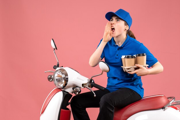 Mensajero femenino de vista frontal sentado en bicicleta con tazas de café en servicio de comida de trabajo de entrega uniforme de color rosa