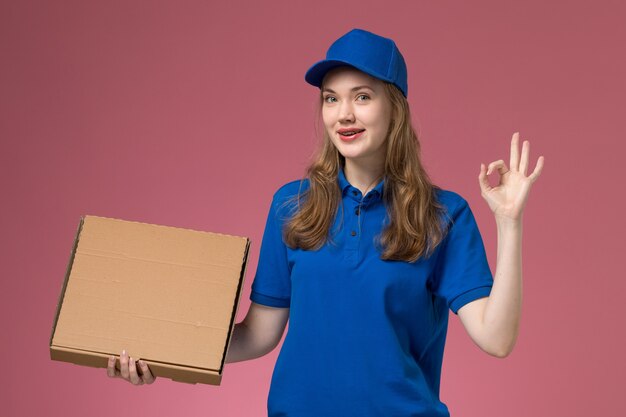 Mensajero femenino de vista frontal en uniforme azul con caja de comida en la empresa uniforme de servicio de trabajo de fondo rosa