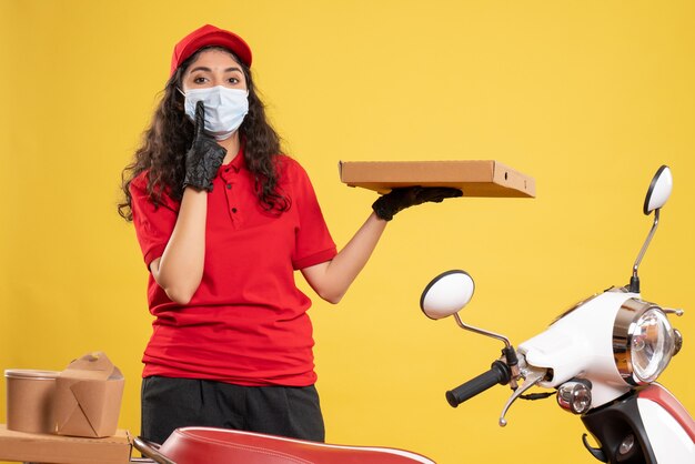 Mensajero femenino de vista frontal en uniforme rojo con caja de pizza en el fondo amarillo trabajador de servicio covid- entrega de trabajo de virus pandémico