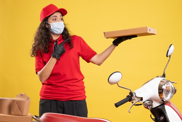 Mensajero femenino de vista frontal en uniforme rojo con caja de pizza sobre fondo amarillo servicio covid- entrega de trabajo de virus pandémico