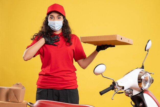 Mensajero femenino de vista frontal en uniforme rojo con caja de pizza sobre fondo amarillo servicio trabajador covid- entrega de trabajo de virus