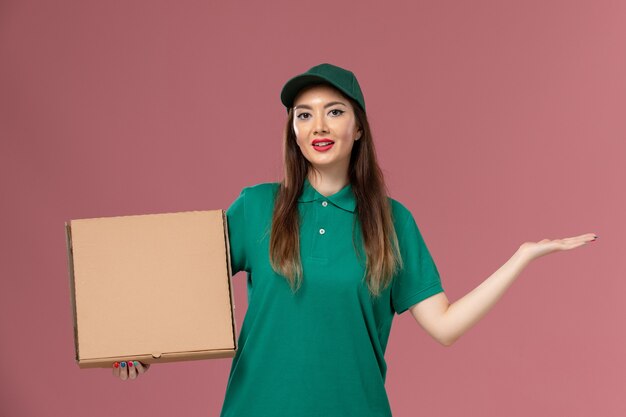 Mensajero femenino de vista frontal en uniforme verde con caja de comida en la pared rosa claro trabajo trabajador servicio entrega uniforme