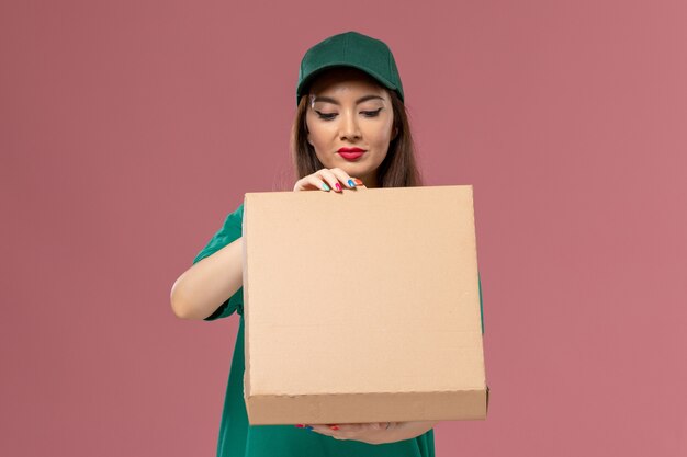 Mensajero femenino de vista frontal en uniforme verde con caja de entrega de alimentos en la empresa de chica de entrega uniforme de servicio de pared rosa