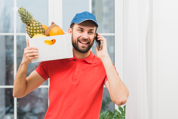 Mensajero con frutas hablando por teléfono