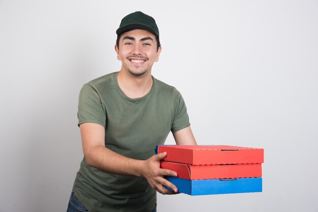 Mensajero joven que lleva tres cajas de pizza sobre fondo blanco.