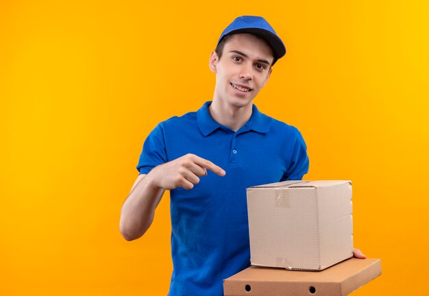 Mensajero joven con uniforme azul y gorra azul apunta a la caja