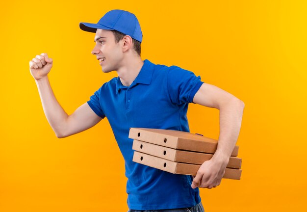 Mensajero joven con uniforme azul y gorra azul corre feliz con cajas en las manos