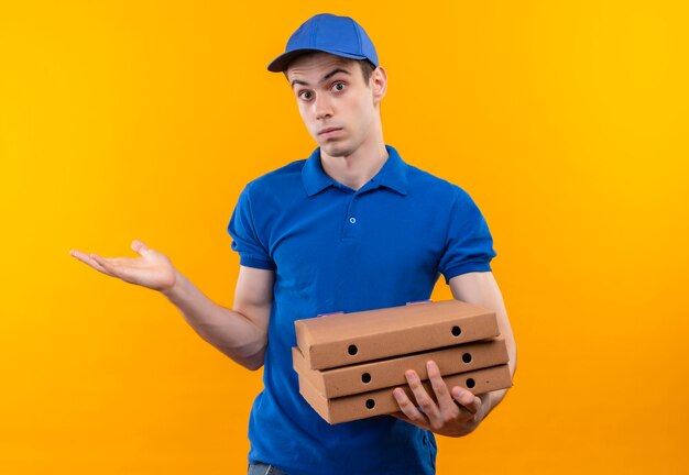 Mensajero joven con uniforme azul y gorra azul haciendo cara confundida y sosteniendo cajas