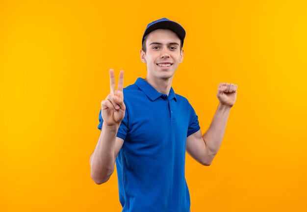 Mensajero joven con uniforme azul y gorra azul haciendo feliz paz y puño
