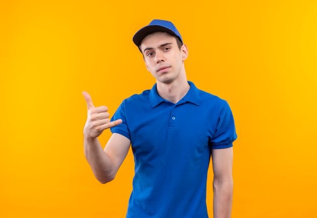 Mensajero joven con uniforme azul y gorra azul muestra el teléfono con los dedos