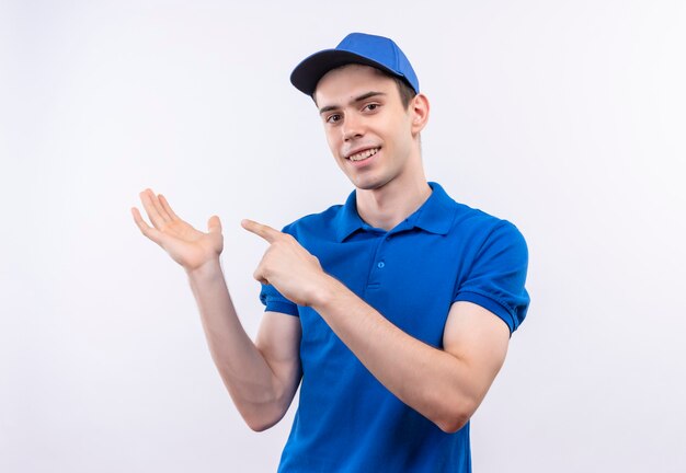 Mensajero joven con uniforme azul y gorra azul sonríe y señala en su mano