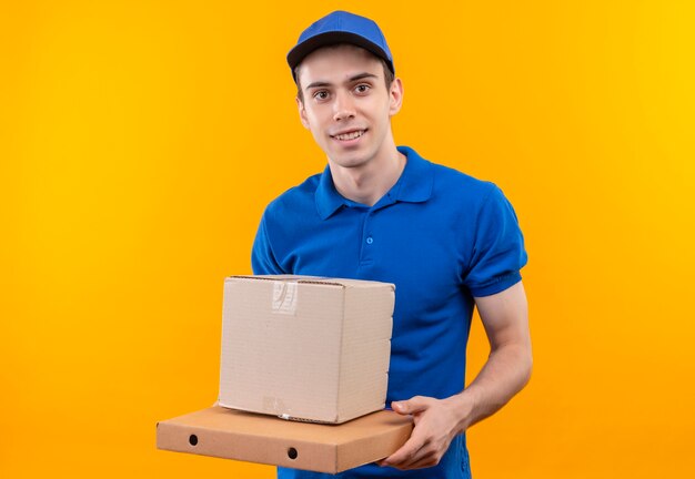 Mensajero joven con uniforme azul y gorra azul sonríe y sostiene la caja