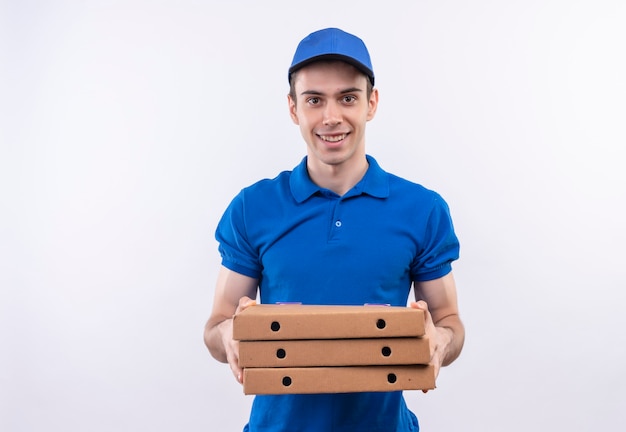 Mensajero joven con uniforme azul y gorra azul sonríe y sostiene cajas