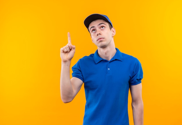 Mensajero joven vestido con uniforme azul y gorra azul haciendo dedo índice confundido