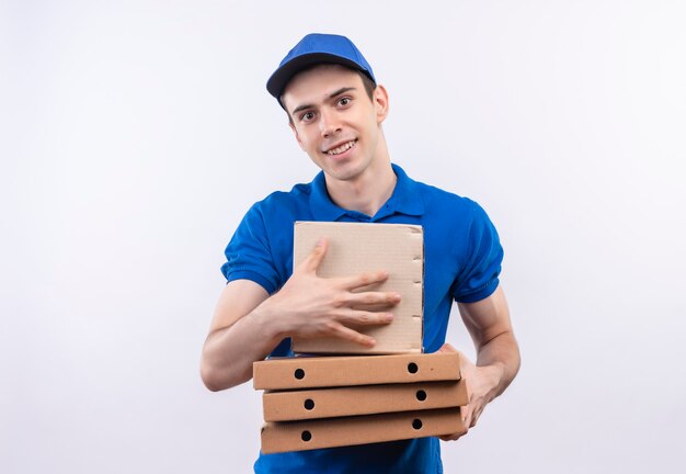 Mensajero joven vistiendo uniforme azul y gorra azul felizmente sostiene cajas