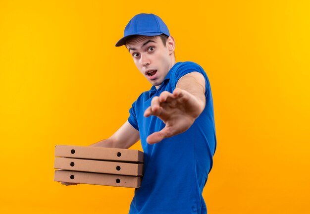 Mensajero joven vistiendo uniforme azul y gorra azul haciendo cara asustada tiene cajas