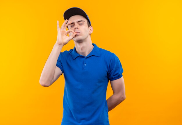 Mensajero joven vistiendo uniforme azul y gorra azul haciendo delicioso con los dedos