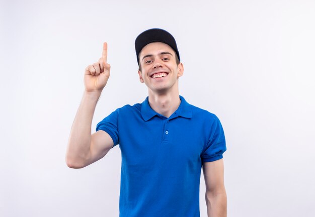 Mensajero joven vistiendo uniforme azul y gorra azul haciendo feliz dedo índice