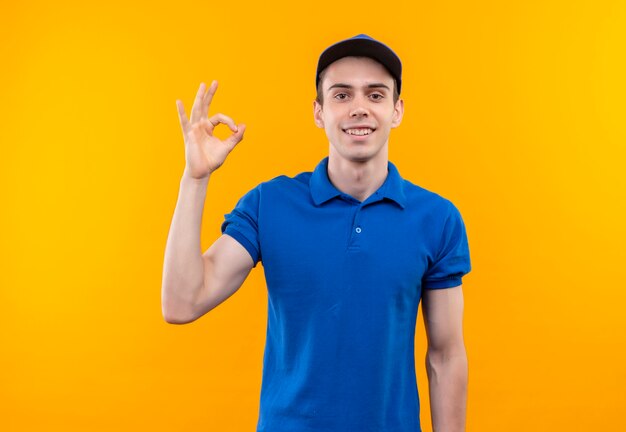 Mensajero joven vistiendo uniforme azul y gorra azul haciendo feliz ok con los dedos