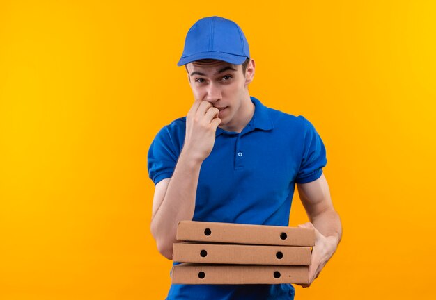 Mensajero joven vistiendo uniforme azul y gorra azul muerde las uñas y sostiene cajas