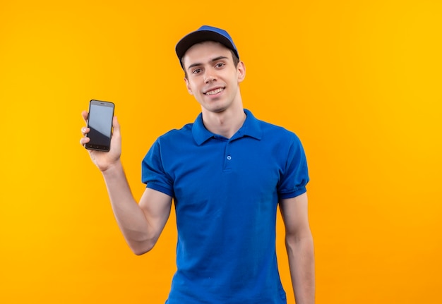 Mensajero joven vistiendo uniforme azul y gorra azul sonriendo sostiene un teléfono