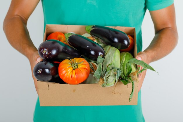 Mensajero masculino en camiseta verde con verduras en caja de cartón