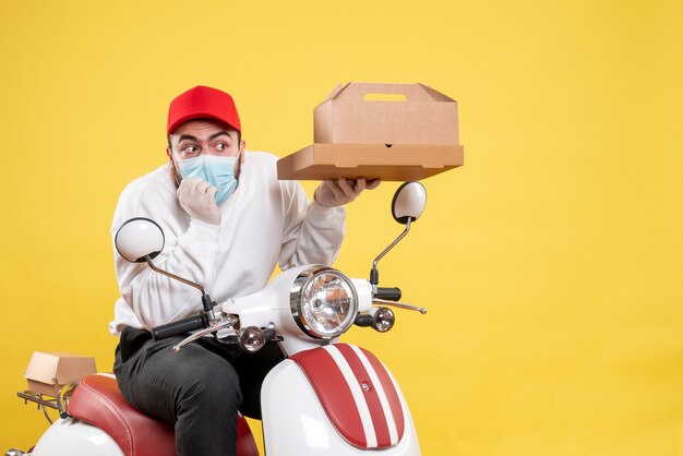 Mensajero masculino en máscara en bicicleta con caja de comida en amarillo