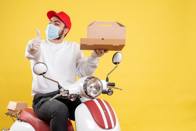 Mensajero masculino en máscara con caja de comida en amarillo