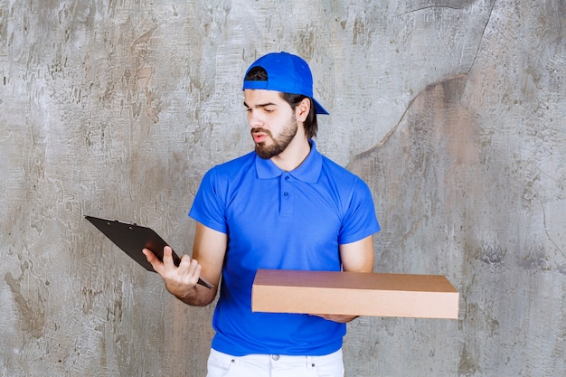 Mensajero masculino en uniforme azul con una caja de cartón y leyendo la lista de clientes.